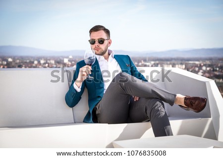 Man millionaire in expensive custom tailored suit, sitting outdoors with glasses and holding a glass of red wine