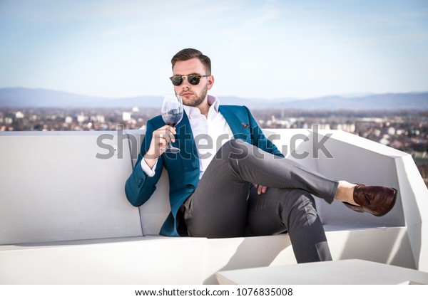 Man\
millionaire in expensive custom tailored suit, sitting outdoors\
with glasses and holding a glass of red\
wine