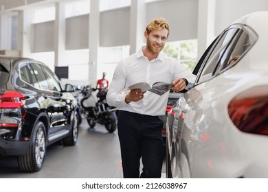 Man Minded Customer Male Buyer Client Wear White Shirt Read Car Papers Documents Agreement Choose Auto Want Buy New Automobile In Showroom Vehicle Dealership Store Motor Show Indoor Sales Concept.