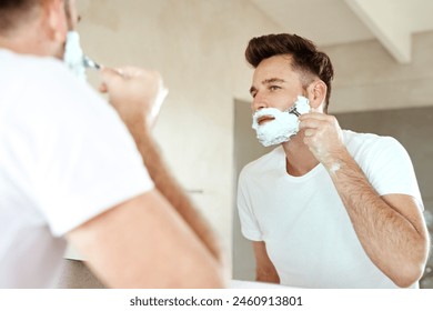 Man, mirror and shaving face with razor in bathroom for grooming, skincare or morning routine. Reflection, foam and person cutting beard for cleaning, health and hair removal for hygiene in home - Powered by Shutterstock