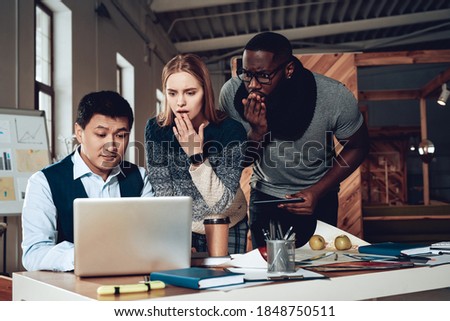 The man was mistaken while doing something in the laptop. Colleagues cover their mouths while looking at the man who works at the laptop. 