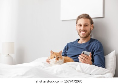 Man With Mobile Phone And His Cute Cat In Bedroom