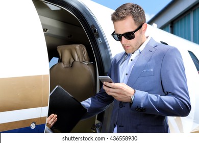 Man With Mobile Phone And Tablet Standing In Door Of Small Jet Plane 