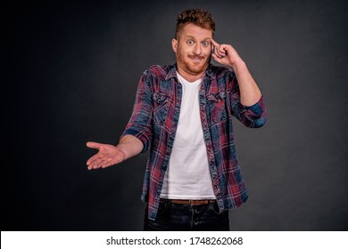 Man mocking friend who made stupid mistake. Portrait of confused and displeased handsome redhead caucasian guy rolling index finger on temple and pointing with palm at camera, acting crazy or dumb.