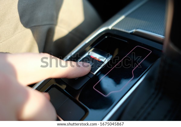 A man in a modern car. Hand presses the auto parking\
button. Close up.