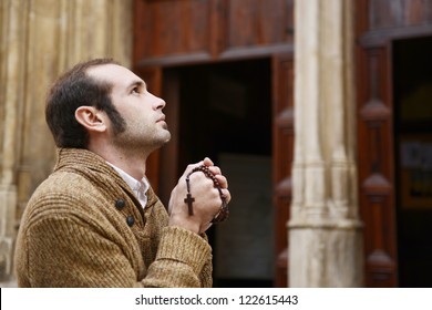 Man or monk praying in front of the church with rosario or prayer beads
