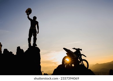 Man with motocross bike against beautiful lights, silhouette of a man with  motocross motorcycle On top of rock high mountain at beautiful sunset, enduro motorcycle travel concept.