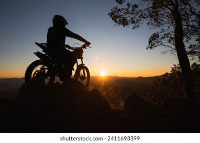 Man with motocross bike against beautiful lights, silhouette of a man with motocross motorcycle On top of rock high mountain at beautiful sunset, enduro motorcycle travel concept.
