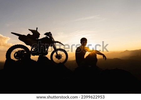 Man with motocross bike against beautiful lights, silhouette of a man with motocross motorcycle On top of rock high mountain at beautiful sunset, enduro motorcycle travel concept.