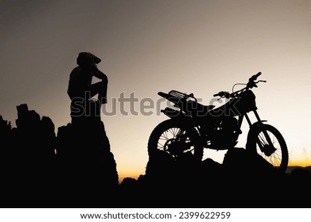 Man with motocross bike against beautiful lights, silhouette of a man with motocross motorcycle On top of rock high mountain at beautiful sunset, enduro motorcycle travel concept.