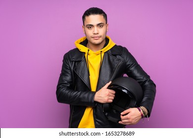 Man With A Motorcycle Helmet Isolated On Purple Background Keeping Arms Crossed