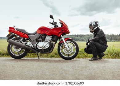 Man Motorcyclist In Helmet Sits In Front Of A Motorcycle And Looks At It