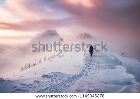 Man mountaineer walking with snow footprint on snow peak ridge in blizzard at morning