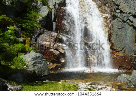 Man in mountains takes shower under cold huge waterfall. Wild nature anforgottable adventure.