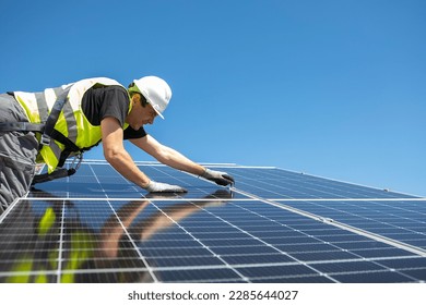 Man mounting modern solar batteries on house's roof. Environment friendly, green energy. Ecological. Using natural renewable energy. Wearing work uniform. High quality photo