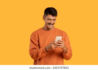 A man with a moustache is holding a cell phone in his hand, looking at the screen with a focused expression. He appears to be typing or scrolling on the device. - Powered by Shutterstock