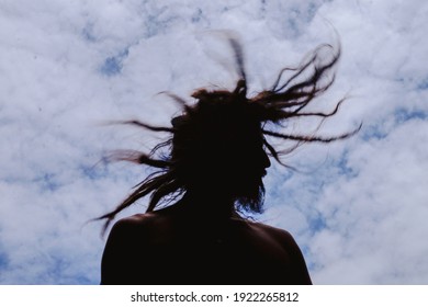 Man moving his hair with dreadlocks with blue sky and clouds in the background