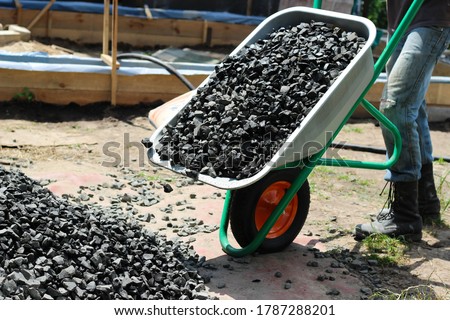 Man moving a wheelbarrow with crushed stones, as part of a building project