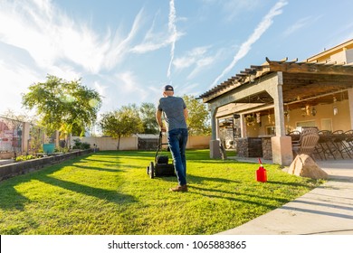 Man Mowing Back Yard In The Bright Mid Day Sun. Fresh Green Lawn With Red Gas Can Resting Near By. 