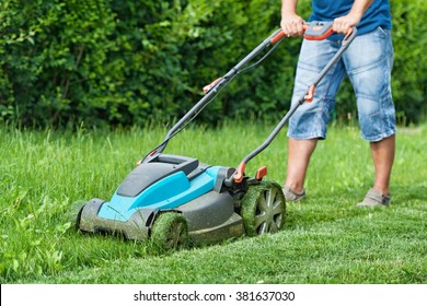 Man mowing the lawn with blue lawnmower in summertime - closeup