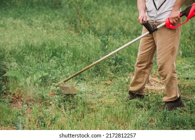 Man Mowing Lawn With Electric Trimmer In The Garden. No Face