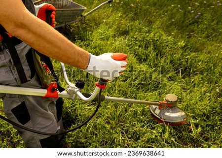 Man mowing tall grass with electric cordless lawn trimmer in backyard. Garden care tools and equipment.