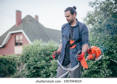 A Man Mows The Grass With A Hand Mower In The Garden. Young Guy Takes Care Of The Lawn And Works In The Garden