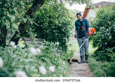 A Man Mows The Grass With A Hand Mower In The Garden. Young Guy Takes Care Of The Lawn And Works In The Garden