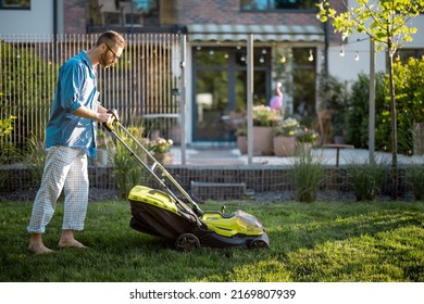Man mows the lawn with lawn mower at backyard of his house. Husband takes care of garden on summer evening. Modern electric wireless garden equipment - Shutterstock ID 2169807939