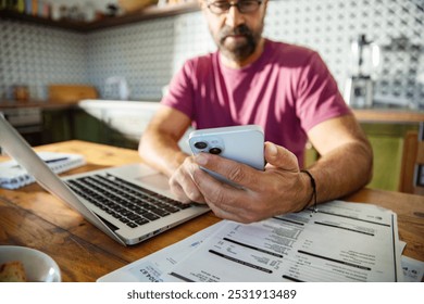 Man multitasking with laptop and phone on kitchen desk at home - Powered by Shutterstock