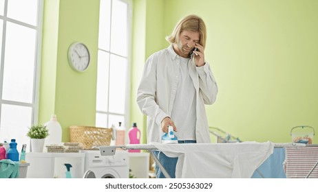 A man multitasks in a bright laundry room, ironing clothes while talking on the phone. - Powered by Shutterstock