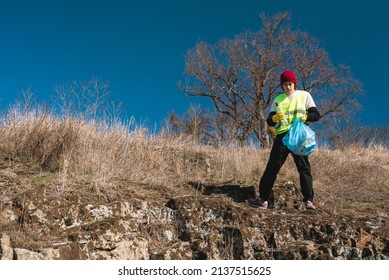 Man Nature Activist In Yellow Vest Puts Glass Bottle In The Blue Trash Bag Outdoors