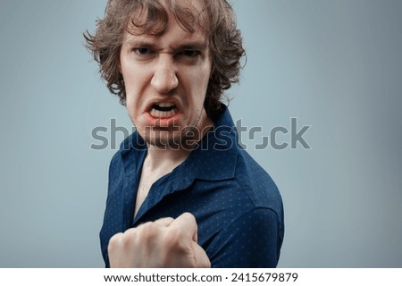 Man in navy shirt expresses intense anger, his clenched fist and grimace speaking volumes of his fury