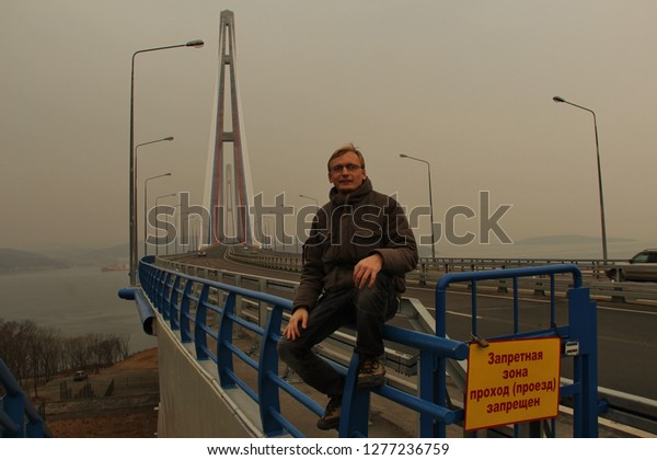 Man near Russky Bridge is cable-stayed bridge in\
Vladivostok, Primorsky Krai, Russia. Bridge connects Russky Island\
and Muravyov-Amursky Peninsula sections. non-English text - pass is\
prohibited.  