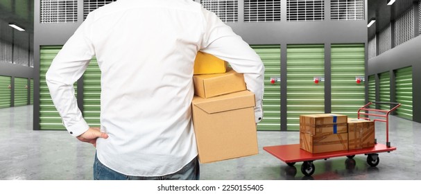 Man near storage room. Guy with boxes back camera. Man in corridors of storage company. Rental storage units. Human looks at closed warehouse containers. Trolley with boxes near businessman - Shutterstock ID 2250155405