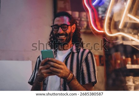 Man in neon lighting laughs while using smartphone, capturing joy, emotional connection and authentic screen engagement in modern digital lifestyle.