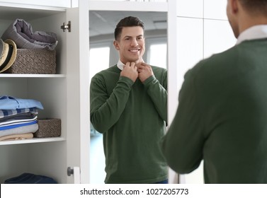 Man In New Outfit Looking At Himself In Mirror Indoors. Fashionable Wardrobe