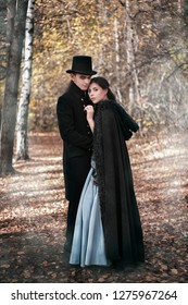 A man in a nineteenth century suit and a woman in a historical dress. Young man and woman in historical costumes in a gloomy forest