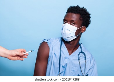 Man Nurse Getting Vaccine Shot With Syringe In Studio. Healthcare Specialist Getting Vaccinated For Coronavirus Immunity. Assistant With Uniform, Face Mask And Stethoscope At Vaccination