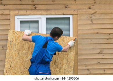 a man obstructs a window with a large piece of plywood before a natural disaster, a hurricane