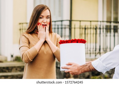 Man offering flower box of red roses to beautiful surprised young woman
