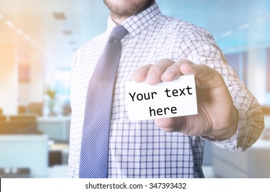Man in office holding a card with a message written on it: Your text here