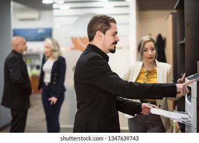 Man In Office Sending Fax Or Printing Files With People In Background