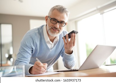 Man In Office Working On Laptop Computer And Using Smartphone