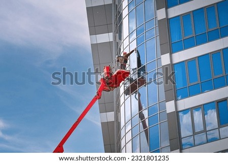 Man on aerial platform washing glass facade at height. Window cleaner, building wet wash. Glass facade cleaning work, workers washing windows at height of high rise building in lifting platform.