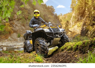 Man on ATV. Off road racing. Quad bike driver in yellow helmet. ATV biker in picturesque place. Man crossed river on quad bike. Guy travel on ATV. Quad bike driver looks around. Extreme sports