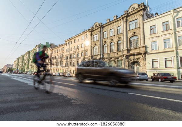 Man on bike and a car moving along\
the sunny street in Saint Petersburg,\
Russia.