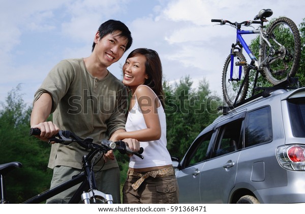 Man on a bike, woman standing next to him, looking\
at camera