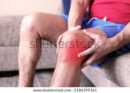 A man on a couch clutching his knee in excruciating pain. Joint pain, arthritis and tendon problems. A person touching the knee at a painful point.