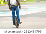 Man on electric monowheel (EUC). Stylish guy moves along sidewalk on mono wheel. Man cross road on electric unicycle, commuting to work. Portable individual transportation vehicle. 